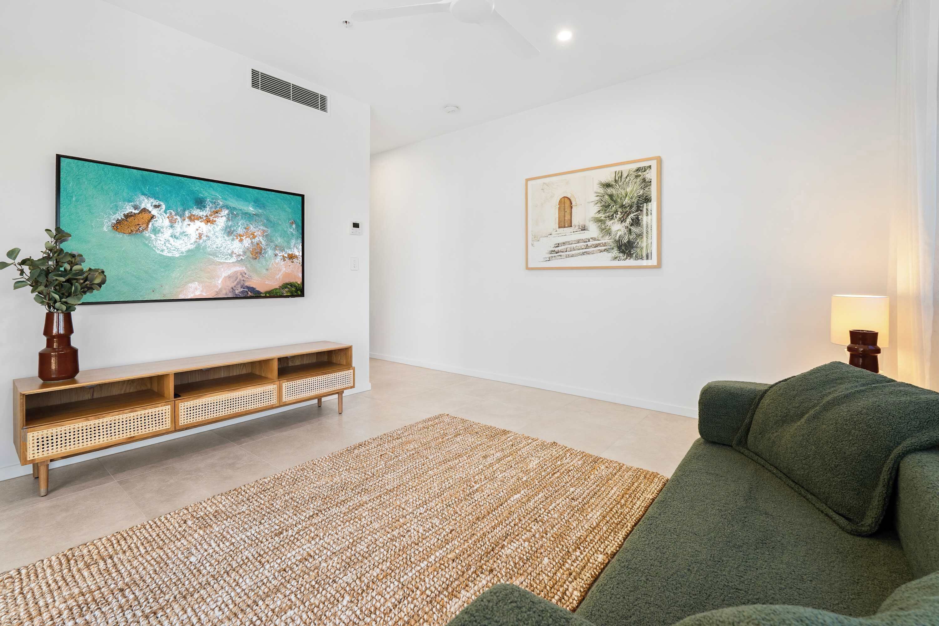 Un salon moderne avec un téléviseur à écran plat, un canapé vert, un tapis tissé et un tableau encadré accroché au mur.