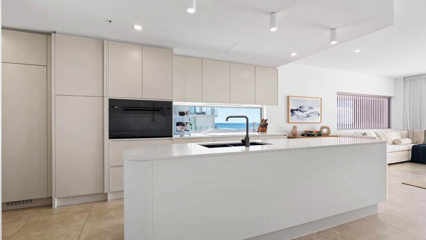 Uma cozinha moderna com uma ilha central, eletrodomésticos embutidos e vista para o exterior.