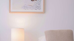 Uma cama bem arrumada com travesseiro branco e manta texturizada, luminária de cabeceira e quadro na parede.