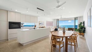 Uma cozinha moderna com uma ilha central, área de jantar com cadeiras de madeira e vista para o oceano.