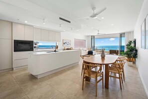 Eine moderne Küche mit einer zentralen Kochinsel, einem Essbereich mit Holzkästen und Blick aufs Meer.
