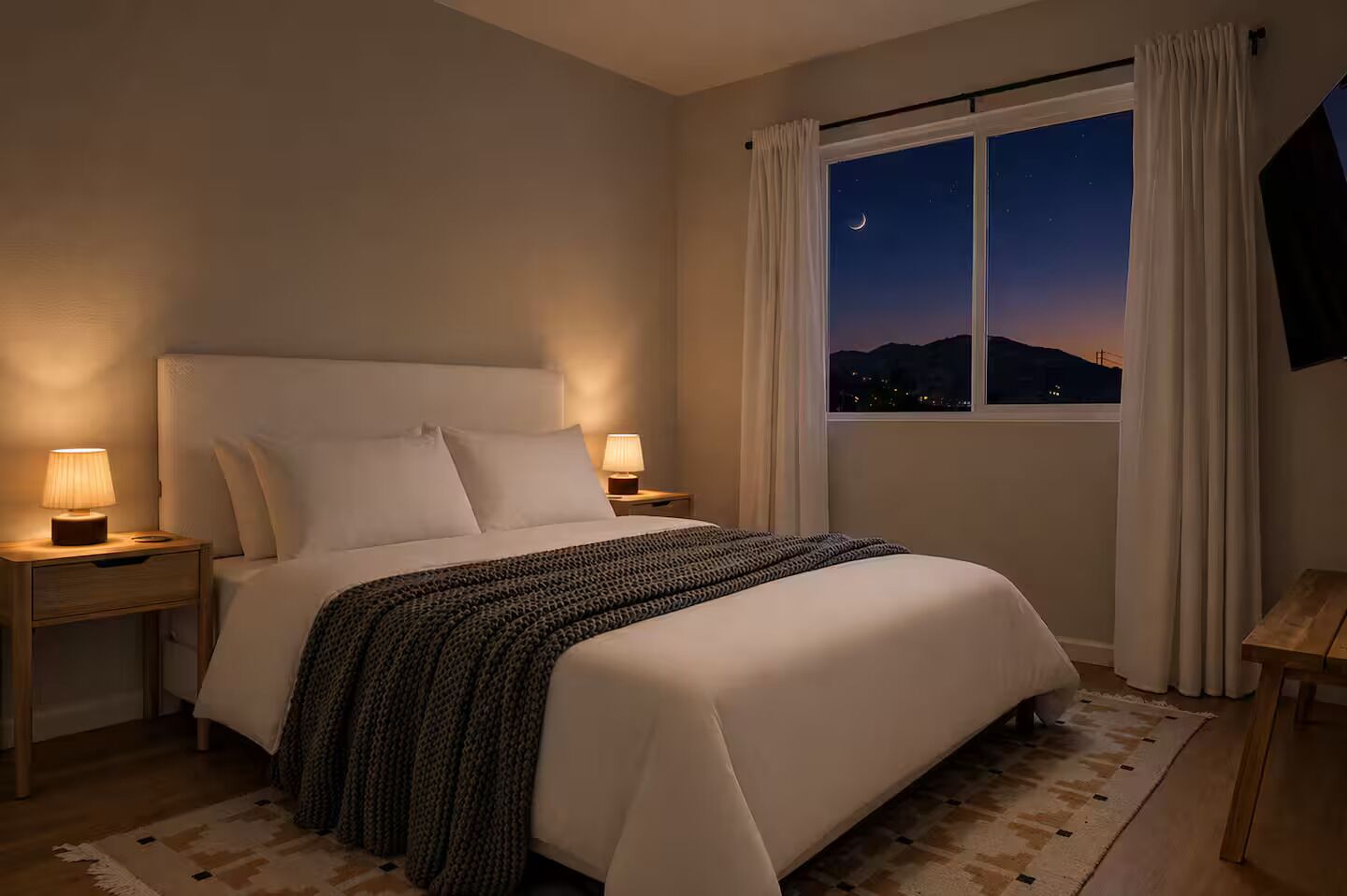 A hotel room with a bed, nightstands, a window with a view of the night sky, and a curtain.