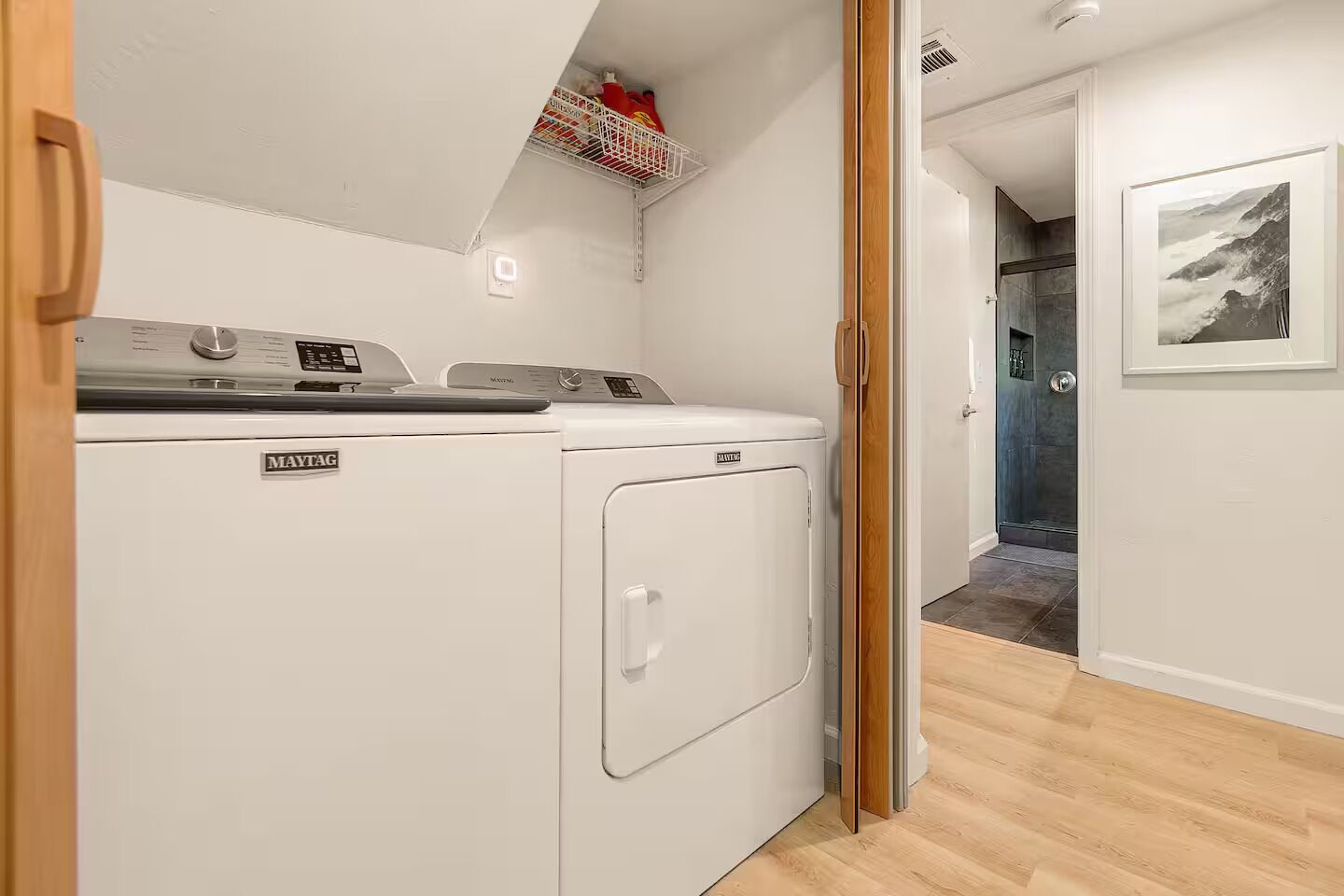 Uma lavanderia com máquina de lavar e secadora Maytag, teto branco e chão de madeira.