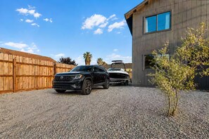A black SUV parked in a driveway with a boat trailer attached, a wooden fence, and a building with a window.