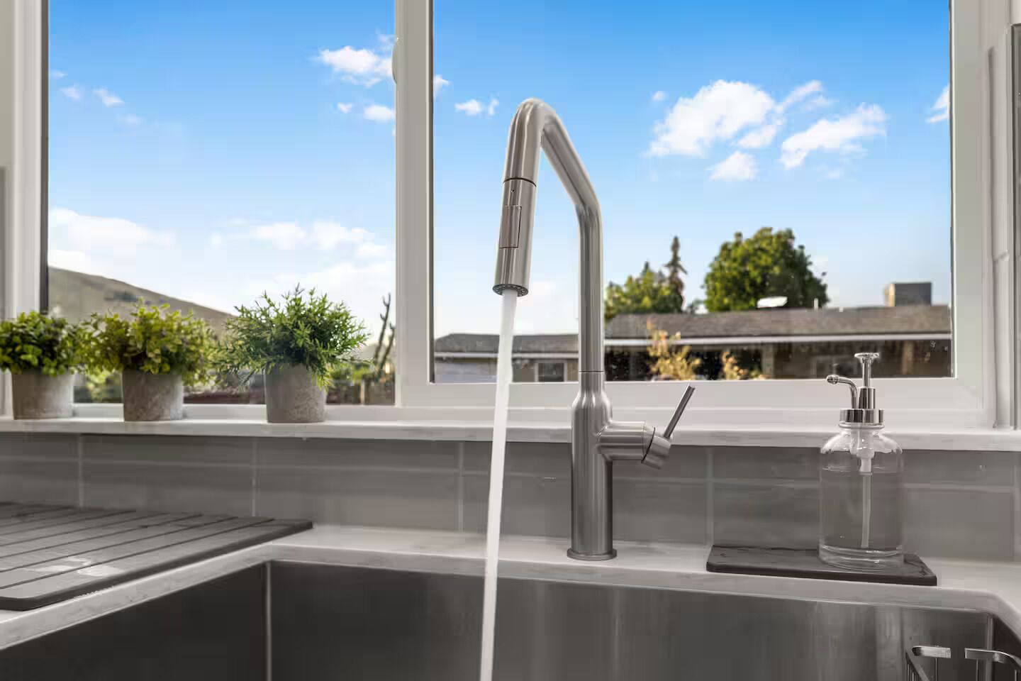 A kitchen sink with a modern faucet, a soap dispenser, and a window with a view of buildings and trees.