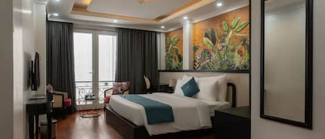 Habitación de hotel con cama, escritorio, silla, balcón y un cuadro grande en la pared.