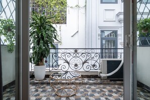 Un balcón con una planta en maceta, barandilla de metal decorativa y suelo de baldosas.