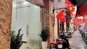 Fachada de edificio con una amplia entrada de vidrio, un cartel que dice 'HANOI BLISS' y varias banderas vietnamitas.