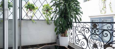 A balcony with a potted plant, a glass table, and a tiled floor.
