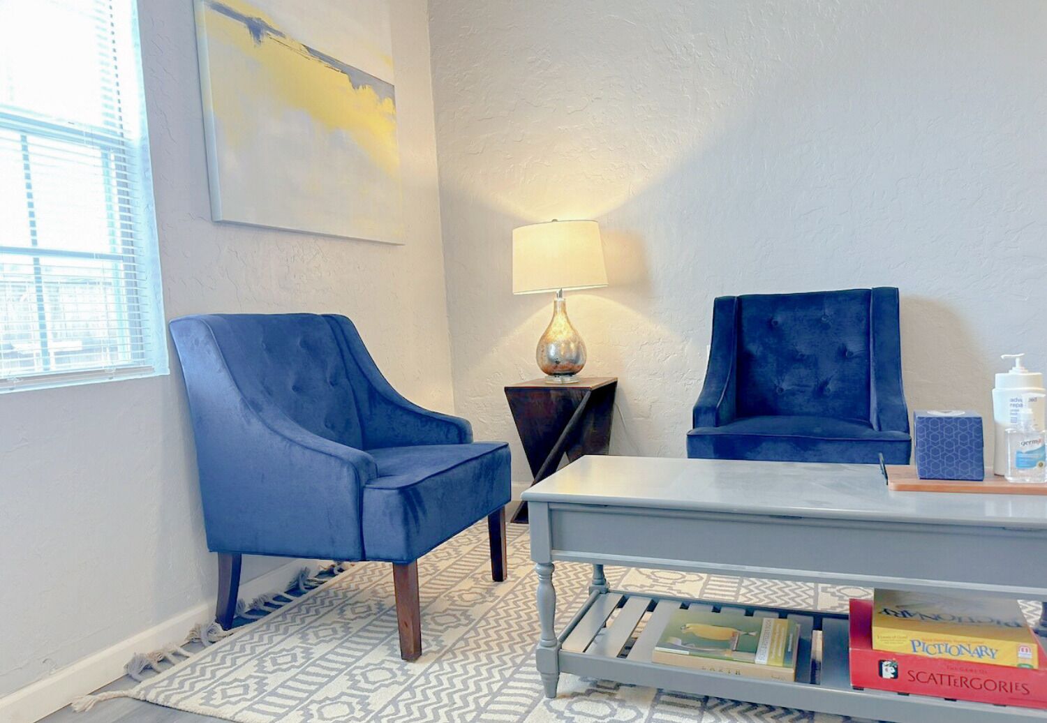 Une pièce avec deux fauteuils bleus, une petite table, une lampe et une bibliothèque remplie de livres.