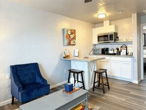 A compact living space with a blue armchair, a small table, and a kitchen area with white cabinets and a microwave. - Roomy 1BR near Integris Children's — a great fit for work stays (Oklahoma City)