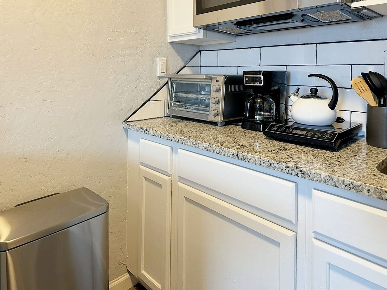 A kitchen with a built-in toaster oven, a coffee maker, and a kettle on the countertop.