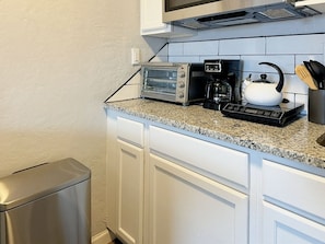 Een keuken met een inbouw toaster, een koffiezetapparaat en een waterkoker op het aanrecht.