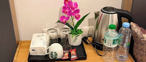 A wooden bedside table with a tray holding a Starbucks cup, a plant, a kettle, and bottled water.