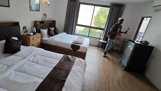 Habitación de hotel con dos camas, un escritorio, una silla, un aparador, una ventana con cortinas y un refrigerador.