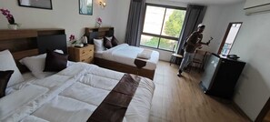 A hotel room with two beds, a desk, a chair, a dresser, a window with curtains, and a refrigerator. - N & B Home Hotel (Bangkok)