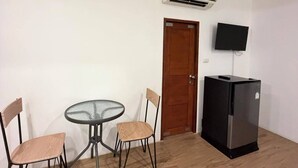 Una habitación con una mesa redonda de vidrio, dos sillas, un refrigerador negro, una puerta de madera y un televisor montado.