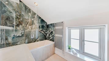 Un baño moderno con pared de mármol, una bañera, una ventana con vistas y una toalla en el alféizar.