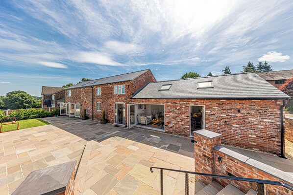 A residential property with a brick exterior, a patio area with stone tiles, and a visible staircase leading to an upper level.