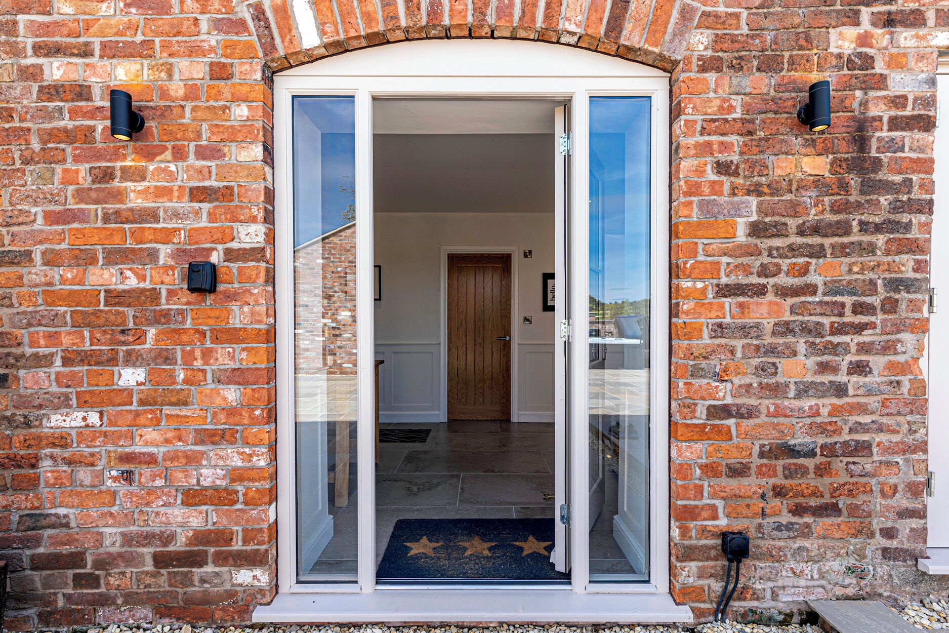 A brick building with a glass door entrance, a wooden door inside, and a star-patterned mat at the entrance.