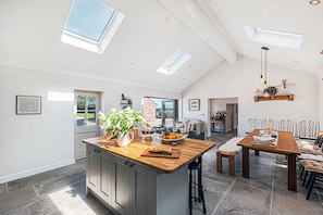 A spacious kitchen with a central island, a dining area with a wooden table and chairs, and a bright interior with skylights. - Fairvale House (Northwich)
