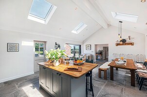 A spacious kitchen with a central island, a dining area with a wooden table and chairs, and a bright interior with skylights.
