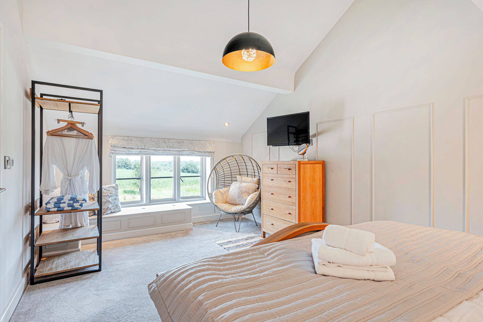 Un dormitorio con cama, una silla colgante, armario, televisor y ventana con vistas a zonas verdes.