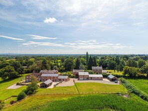 A large estate with multiple buildings, expansive green fields, and a clear sky. - Fairvale House (Northwich)