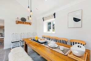 Un comedor con una mesa de madera, sillas blancas, un reloj y una ventana con vistas.