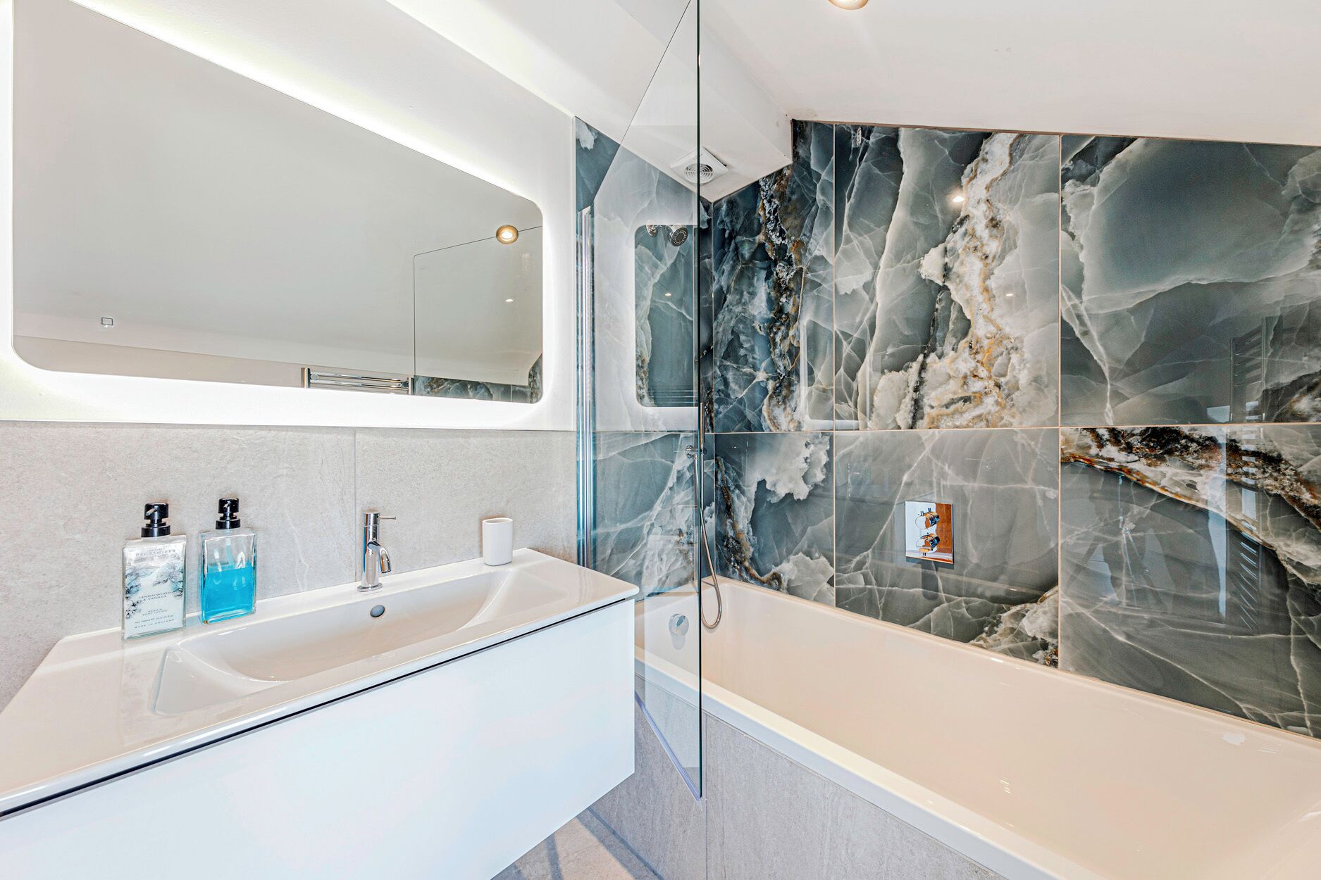 Un baño moderno con ducha envuelta en vidrio, un lavabo blanco y paredes con diseño de mármol.
