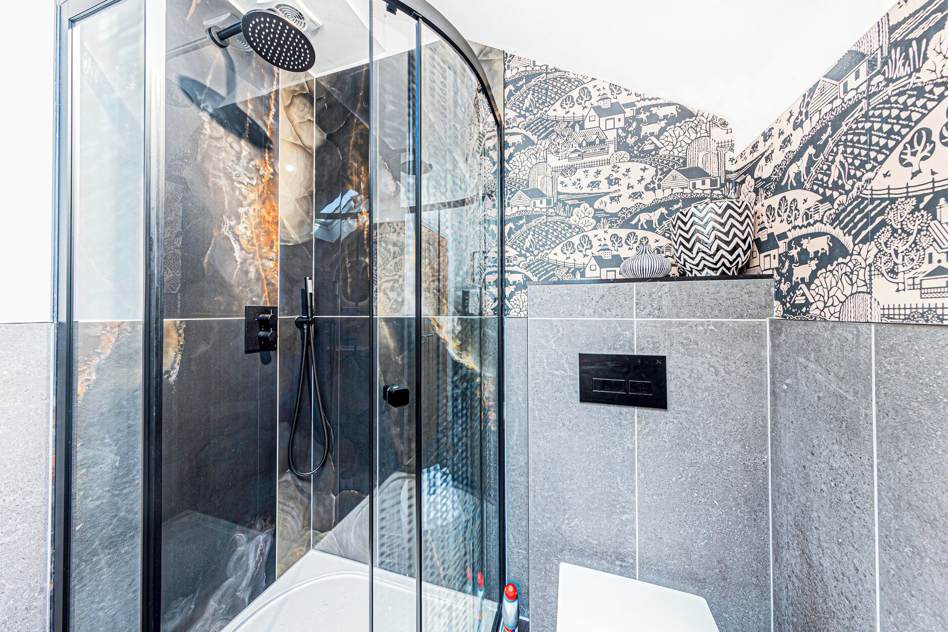 Un baño moderno con ducha envuelta en vidrio, una bañera blanca y un muro de azulejos con un mural detallado.
