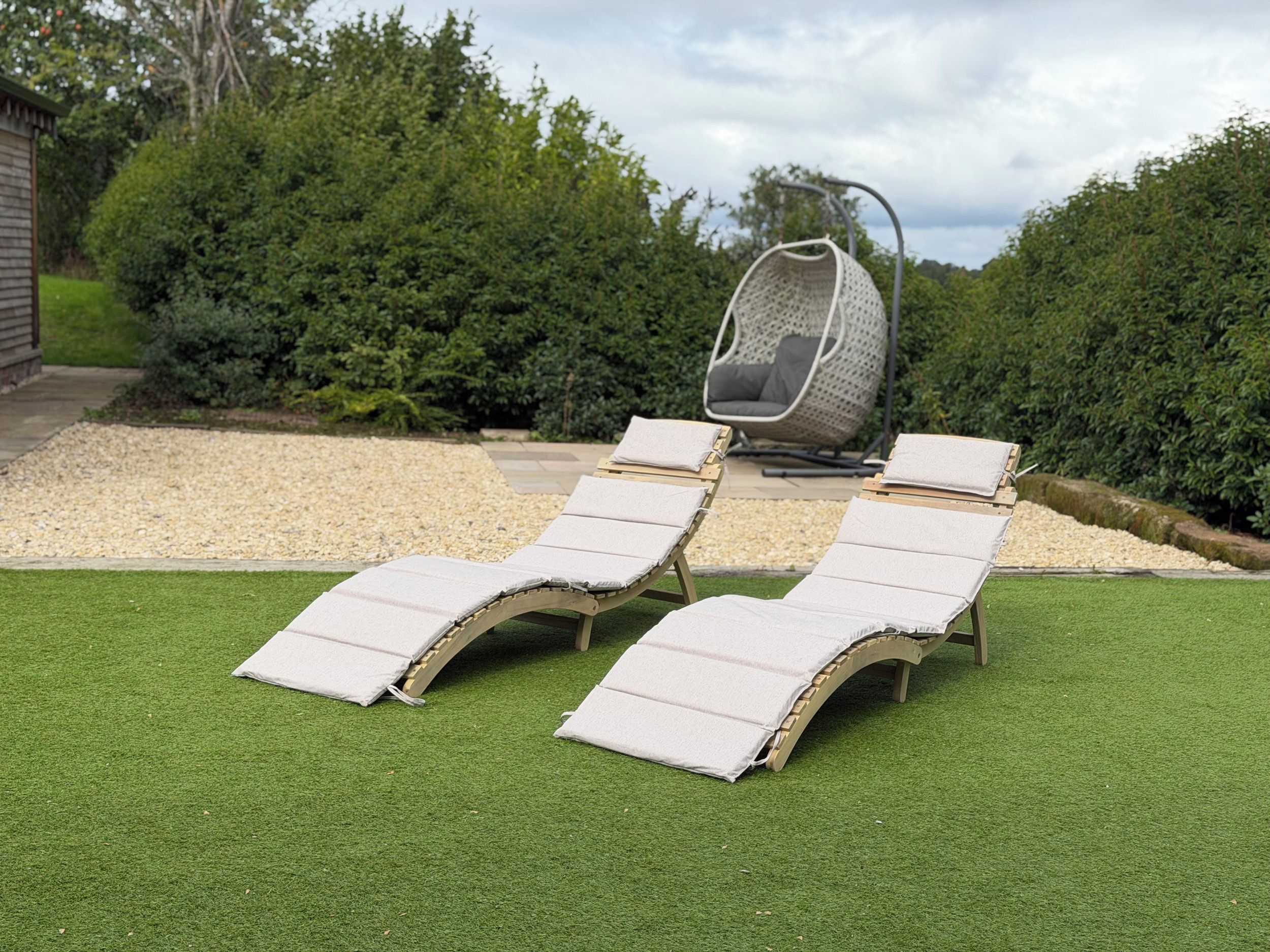 Un jardín con césped artificial, dos sillones de descanso y una silla colgante.