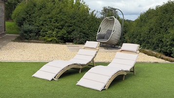 Un jardín con césped artificial, dos sillones de descanso y una silla colgante.