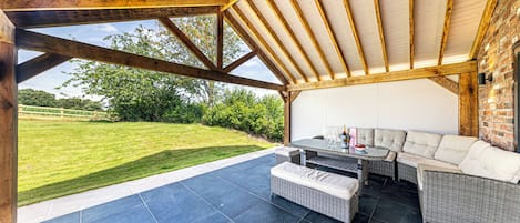 An outdoor patio with a wooden ceiling, a dining table, and a sofa.
