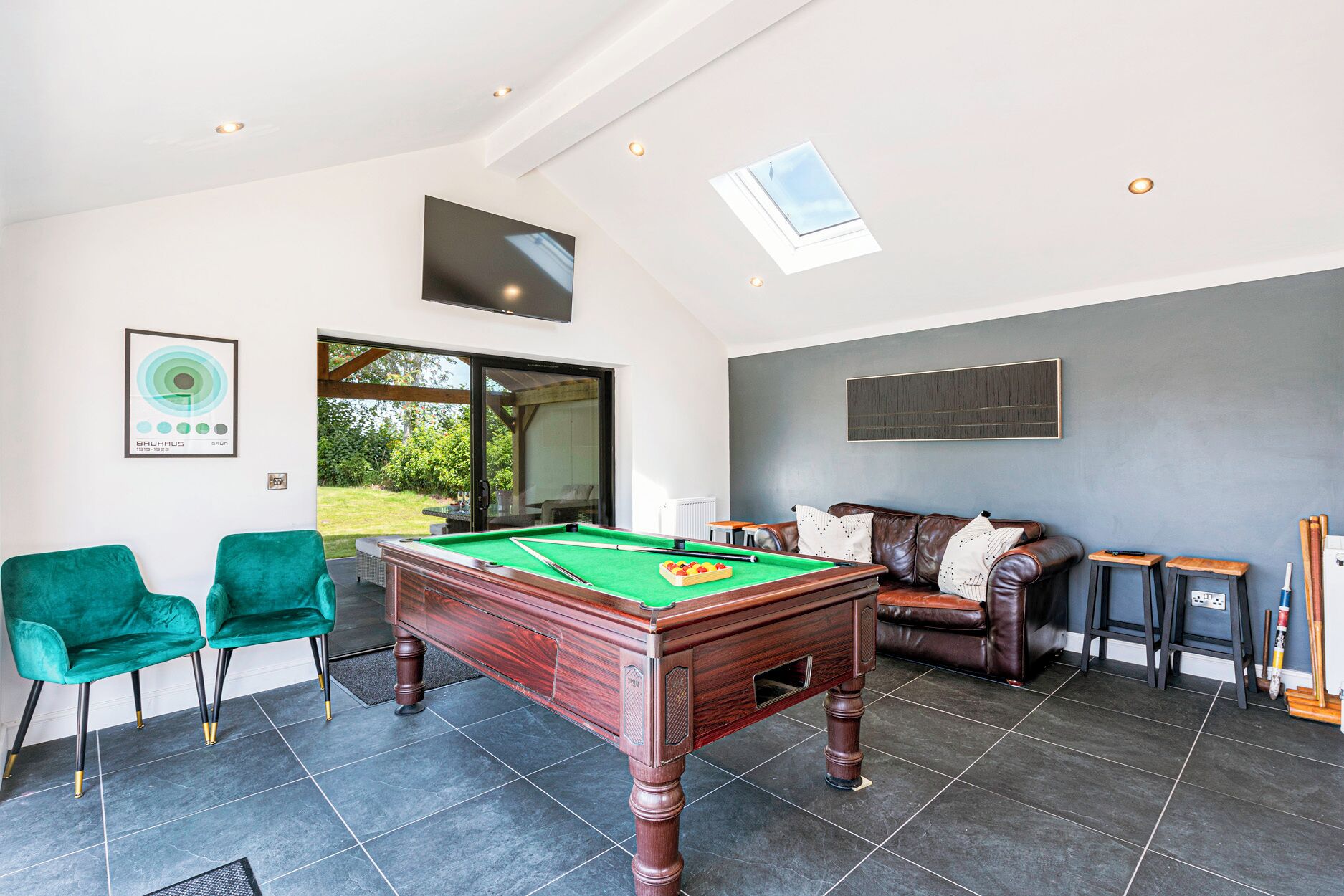 A billiards table in a room with a sofa and chairs, a window, and a framed picture on the wall.