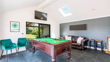 A billiards table in a room with a sofa and chairs, a window, and a framed picture on the wall.