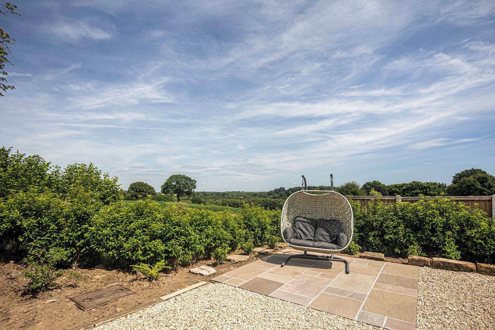 Jardín con zona de estar, que incluye una silla con respaldo tejido y un cojín.
