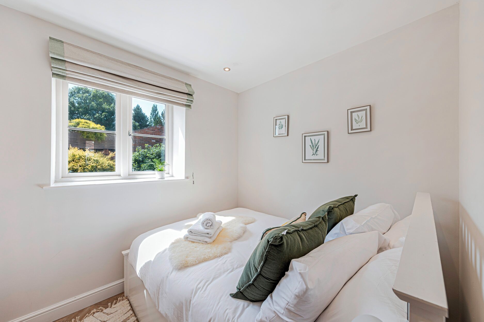 A bedroom with a bed, a window with blinds, and framed botanical prints on the wall.