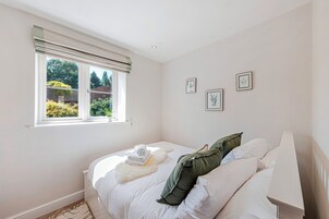 Un dormitorio con cama, ventana con persianas e impresiones botánicas enmarcadas en la pared.