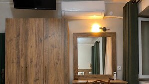 Una habitación con un armario de madera, un escritorio con silla, un televisor de pantalla plana montado en la pared y un equipo de aire acondicionado.