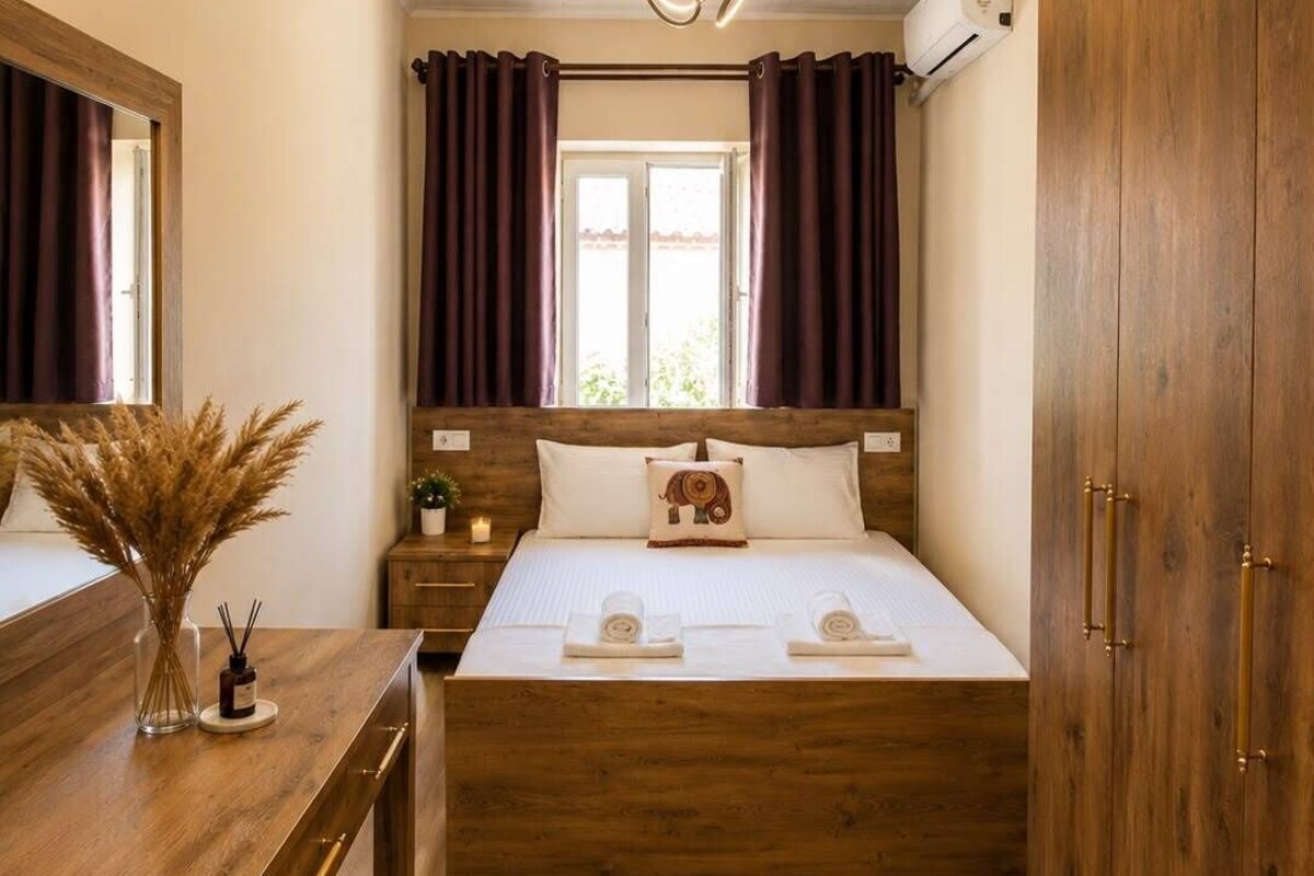 A bedroom with a wooden bed, a bedside table with a vase and candles, a mirror, and a wardrobe.