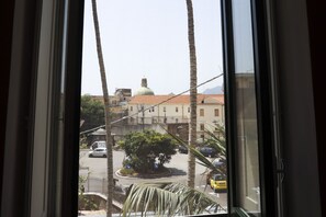 Vista a través d'una finestra, amb una palmera i un edifici amb cúpula al fons.
