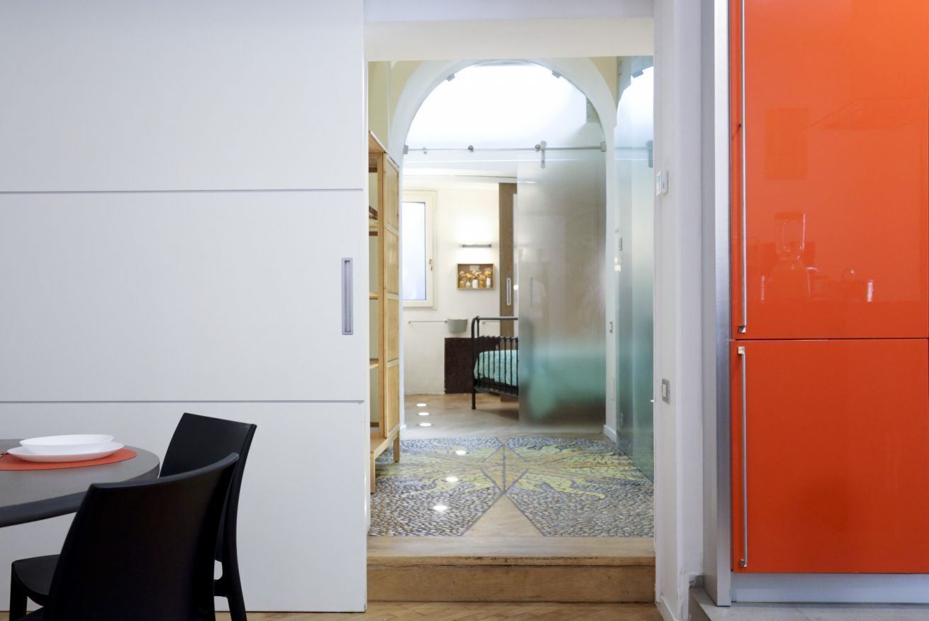 Una cocina moderna con comedor, una puerta de vidrio que da a un dormitorio y un refrigerador naranja brillante.