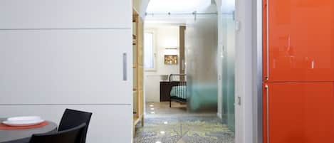 A modern kitchen with a dining area, a glass door leading to a bedroom, and a bright orange refrigerator.