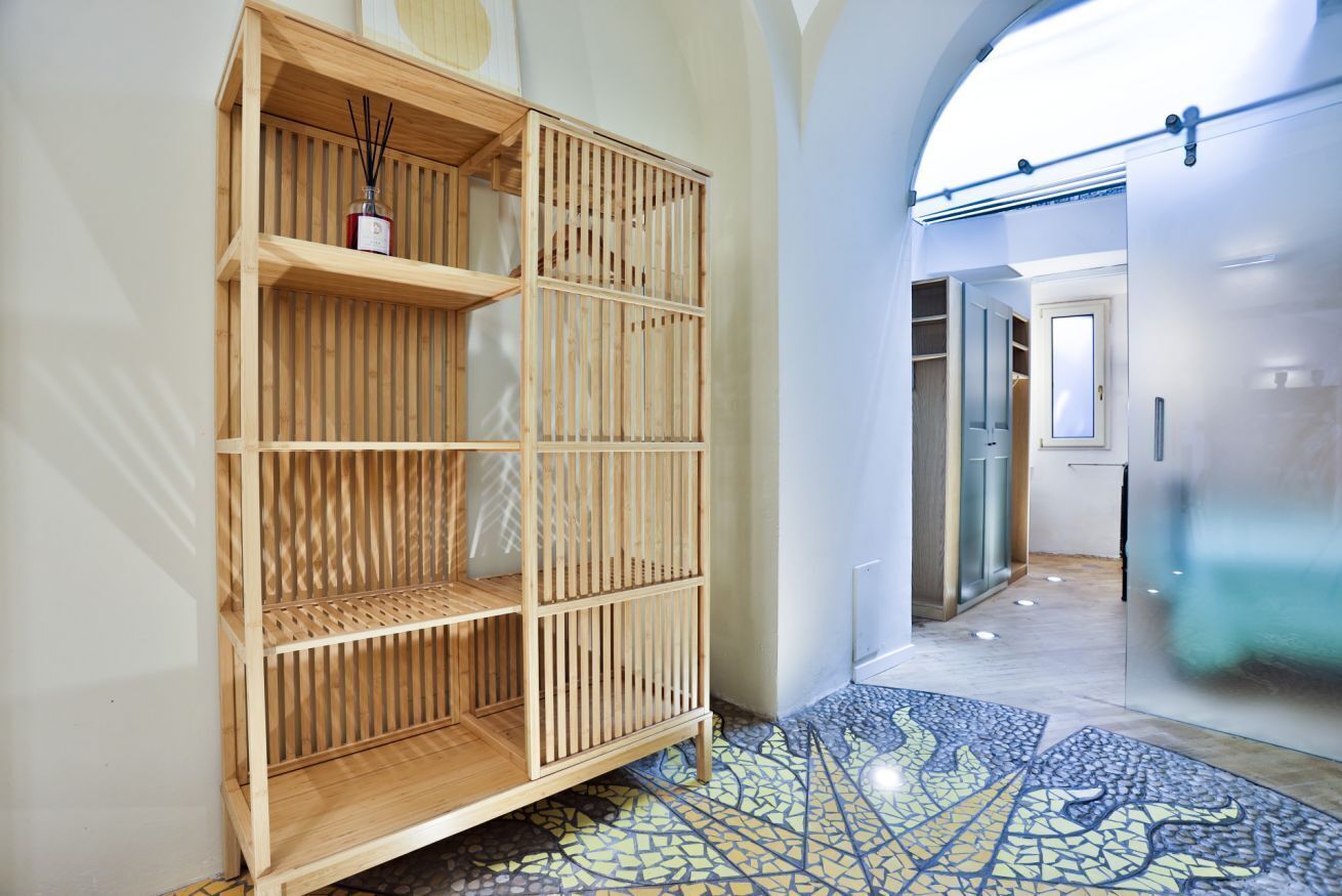 Un interior modern amb una estanteria de fusta, un paviment de rajoles i un passadís que condueix a una habitació amb una porta de vidre.
