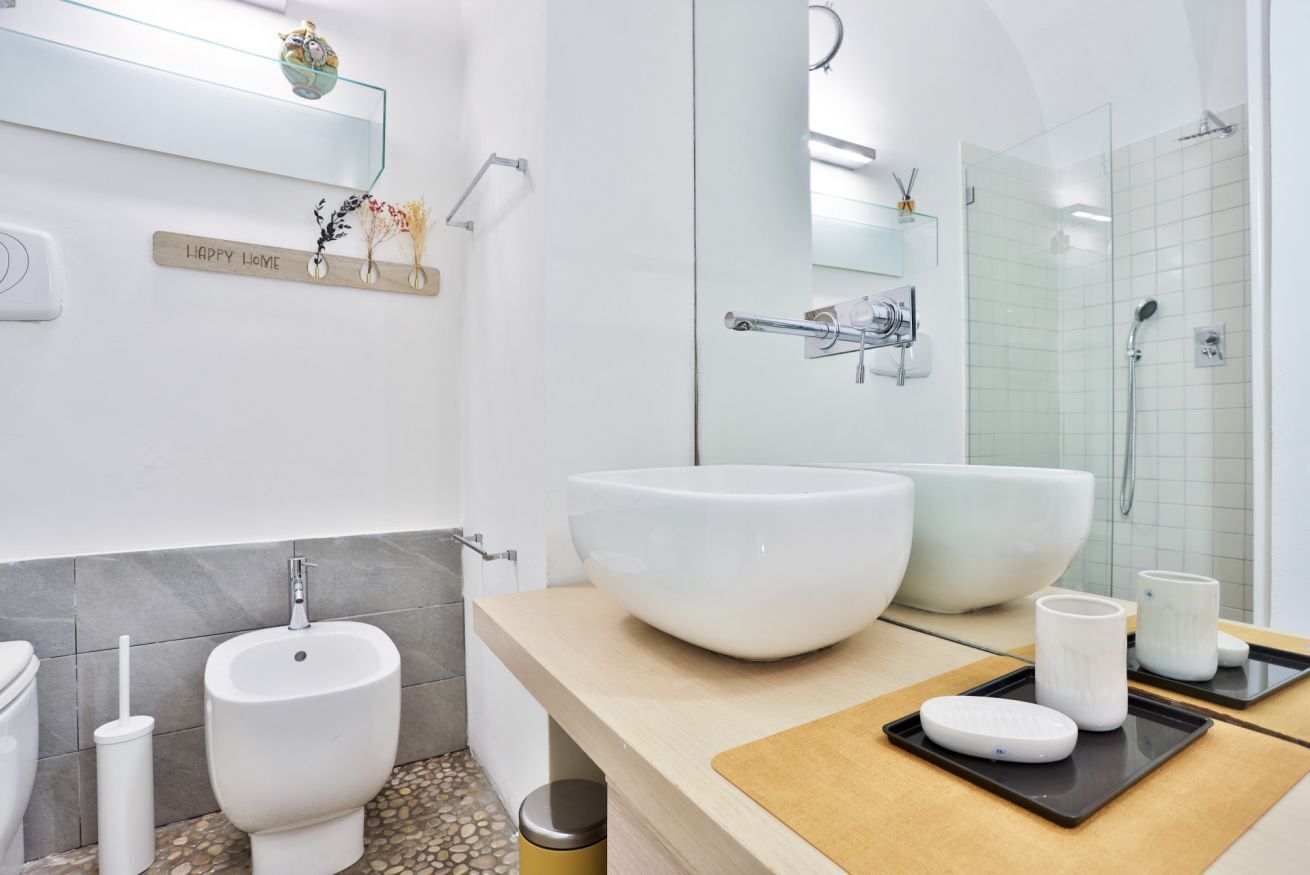 A modern bathroom with a large white sink, bidet, and a glass-enclosed shower.