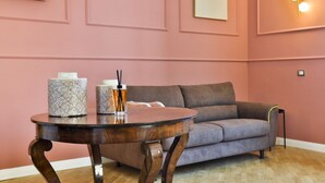 Um quarto com uma mesa de madeira redonda, um sofá cinzento e uma luminária fixada na parede.