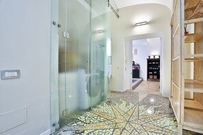 Un passadís amb una porta de vidre que dona a un bany, un sòl de rajola i una prestatgeria de fusta amb objectes a dins.