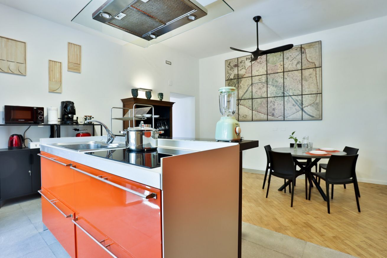 Uma cozinha moderna com uma ilha central, uma área de jantar com mesa e cadeiras, e um ventilador de teto.