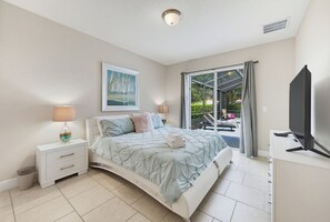 Ein Schlafzimmer mit einem Bett, Nachttischen, einer Lampe, einem Gemälde, einem Fenster mit Vorhängen und einem Fernseher.